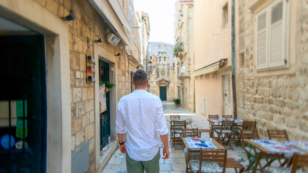 Tourist walking down a narrow cobblestone street in Dubrovnik Old Town, with outdoor café tables and historic stone buildings