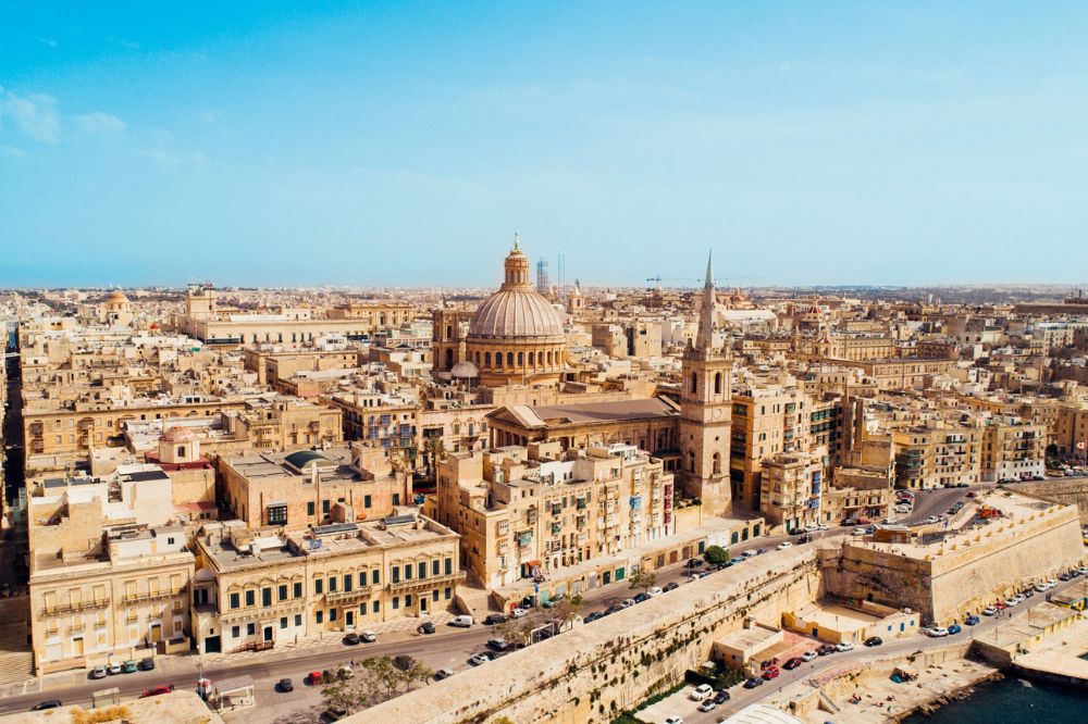 Valletta seen from above, featuring brown and orange architecture beneath a vibrant blue sky.