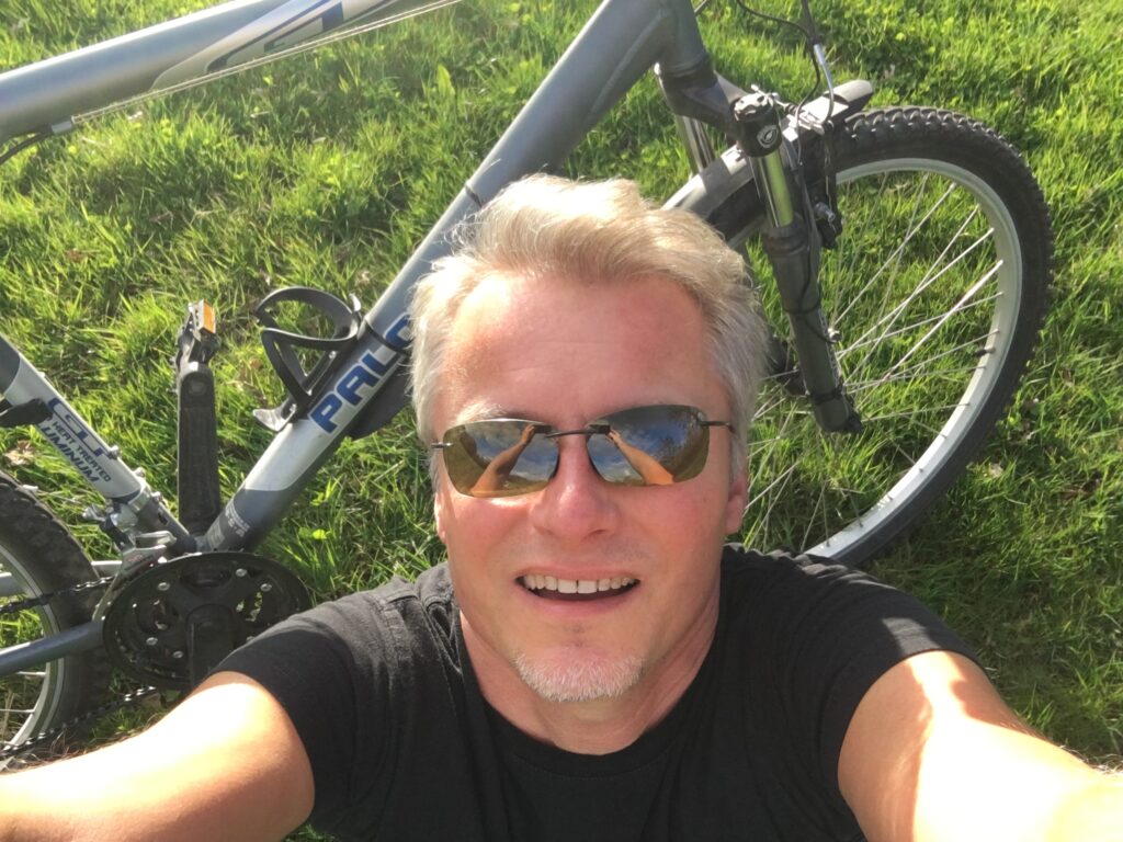 Smiling cyclist taking a selfie with a bicycle on green grass during a sunny day near Lake Balaton, Hungary
