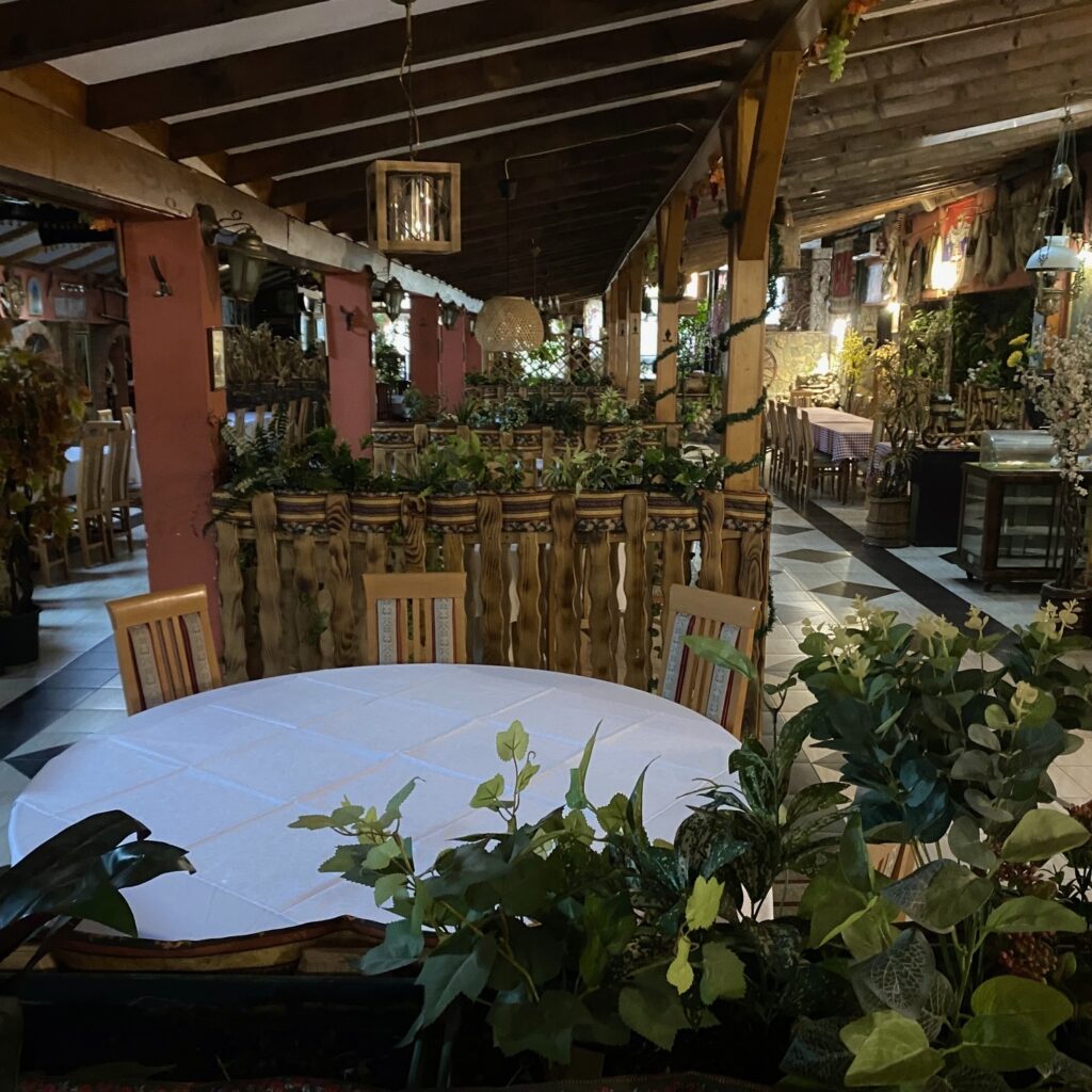 Dining room at Čačanin restaurant in Belgrade with wooden decor, plants, white tablecloths, and a traditional atmosphere.