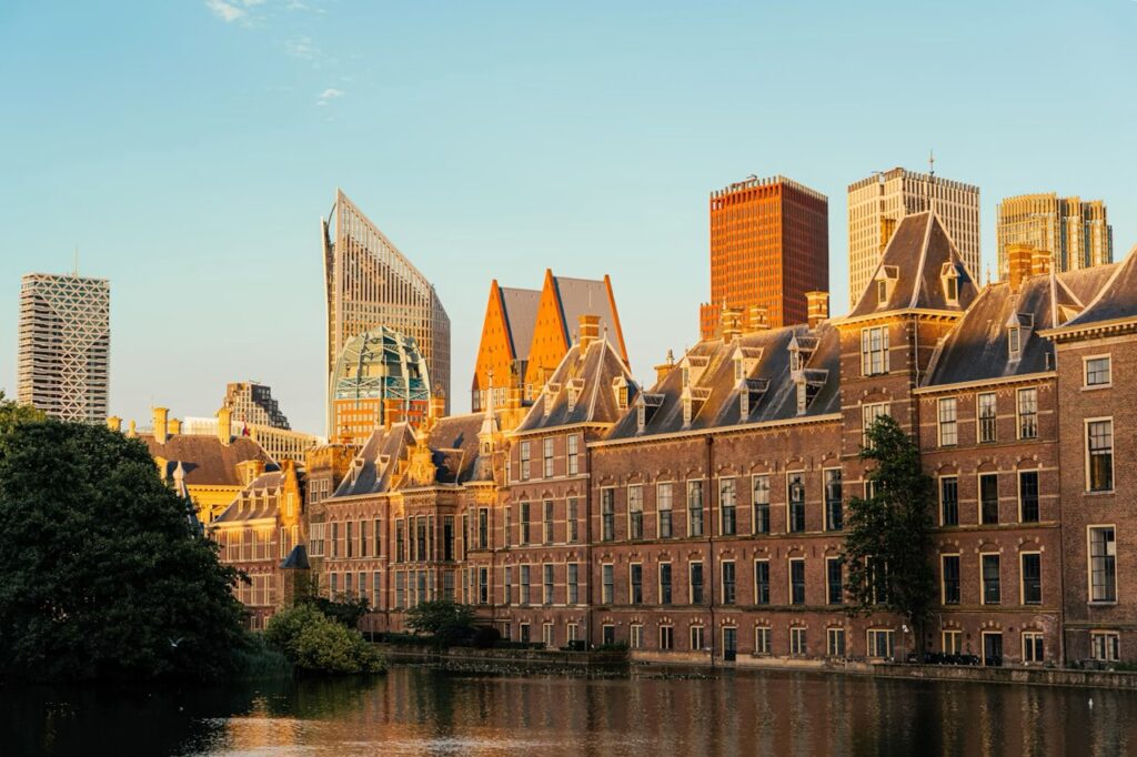 Historic buildings and modern towers in The Hague reflected in the water at sunset.