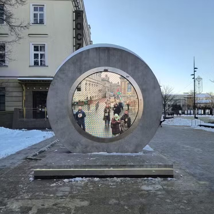 The Portal art installation on a snowy street in Lublin, with people appearing on its circular digital screen.