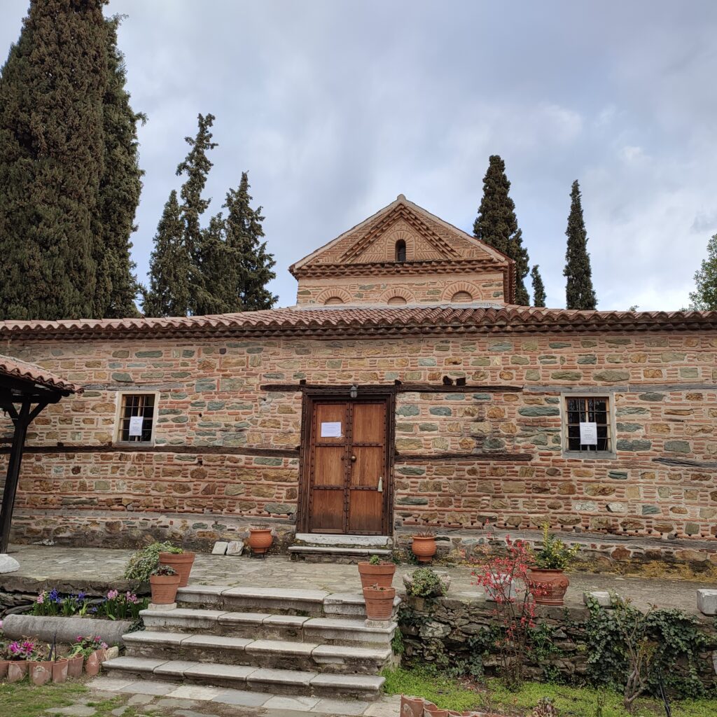 Church of St. Nicholas Orphanos. ©ThanasisKoukopoulos_ Exterior of the Church of St. Nicholas Orphanos in Ano Poli, Thessaloniki, with brick walls, wooden doors, and a garden.