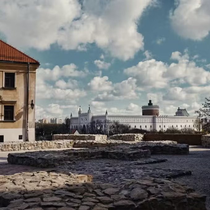Historic stone foundations at Po Farze Square with Lublin Castle visible under a cloud-filled sky.