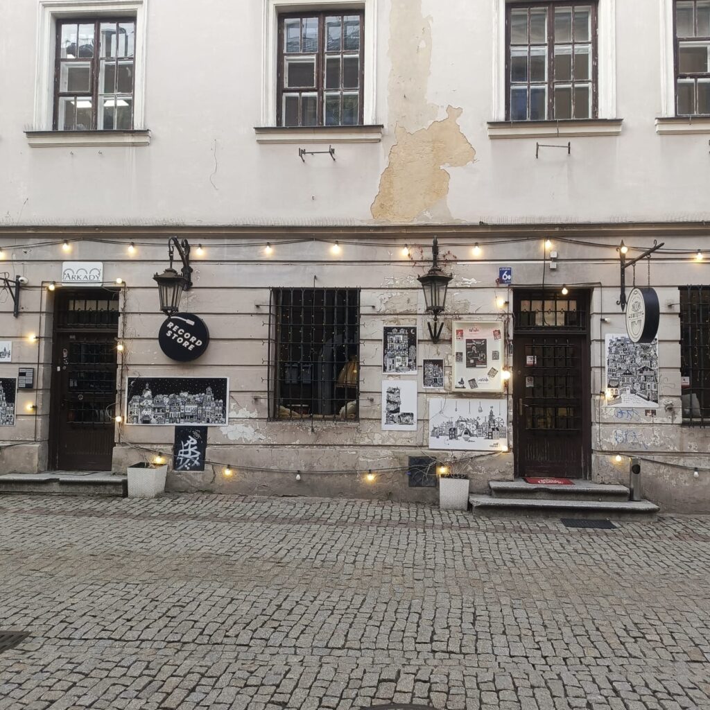 String lights, artwork, and a record store entrance on a cobblestone street in Lublin’s Old Town.